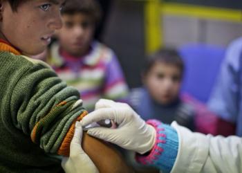 This Wednesday, Dec. 18, 2013 photo shows a Syrian boy watching as UNICEF nurse Genivieve Bashalani prepares him for a measles vaccination at the U.N. refugee agency's registration center in Zahleh, in Lebanon's Bekaa Valley. With an endless surge of refugees now fighting the bitter winter cold, humanitarian organizations are struggling to find new ways to reach refugees with the timely, accurate information they need to survive, including the recruitment of refugees as volunteers so that people can access information from sources they can trust.(AP Photo/Maya Alleruzzo)