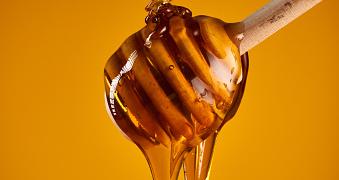 Closeup of honey dripping off a wooden dipper, isolated on yellow background