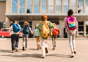 Little kids schoolchildren pupils students running hurrying to the school building for classes lessons from to the school bus. Welcome back to school. The new academic semester year start