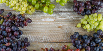 Ripe grapes on wooden background, flat lay.